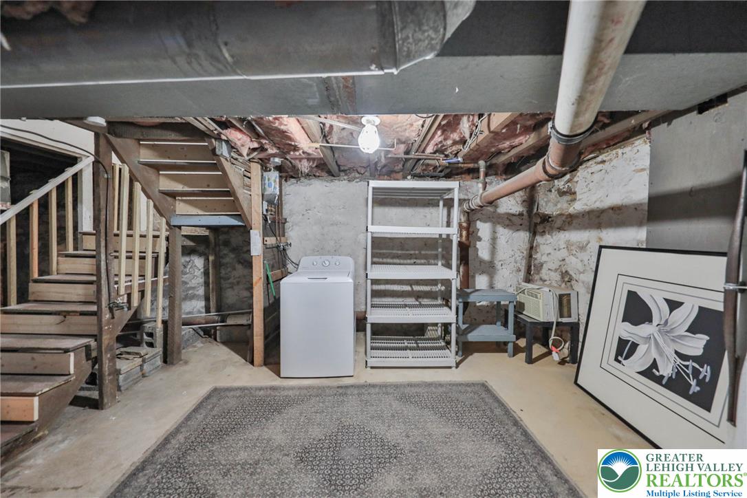 Basement with exposed pipes, wooden stairs, a washing machine, and metal storage shelving.