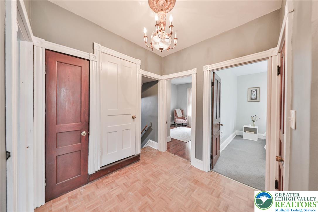 Hallway with parquet flooring, ornate white trim, a chandelier, and open doorways to adjoining rooms.