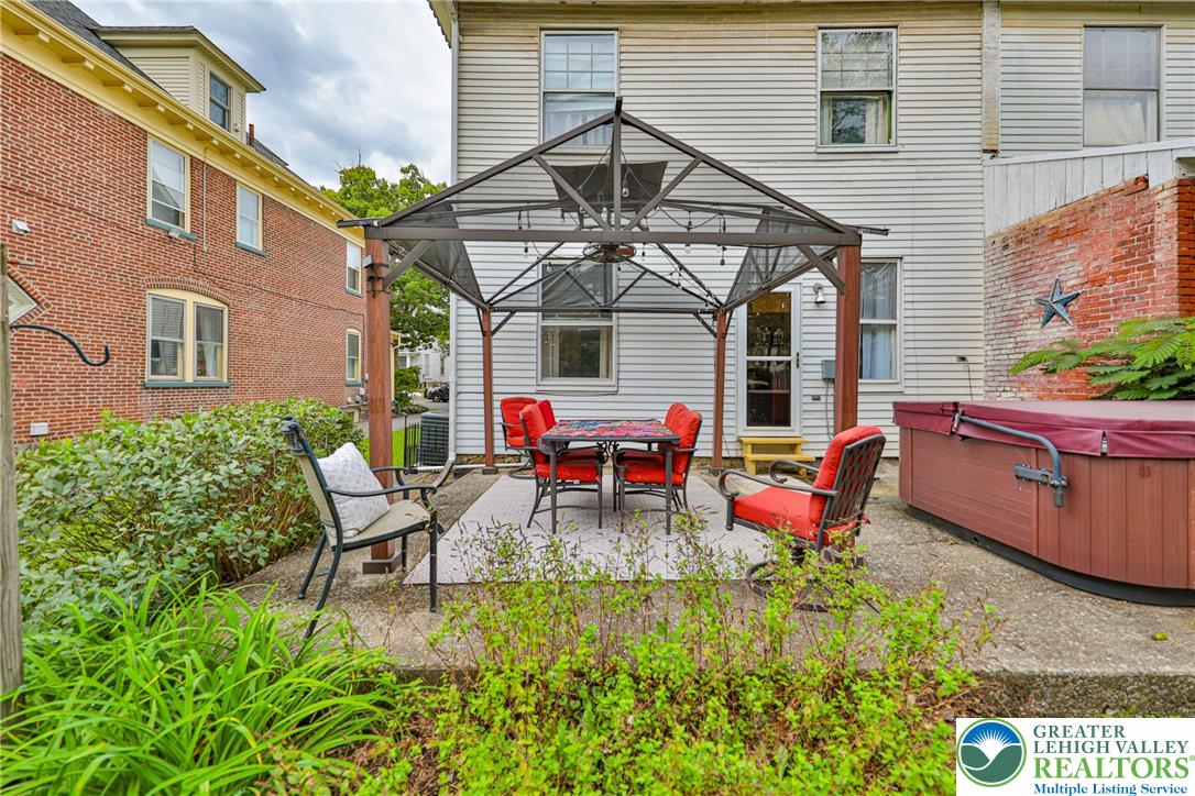 Backyard patio with a metal-framed canopy, red dining chairs, and a covered hot tub.