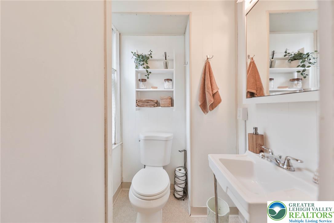 Bathroom with a white toilet, built-in shelves, and a sink vanity with mirror.