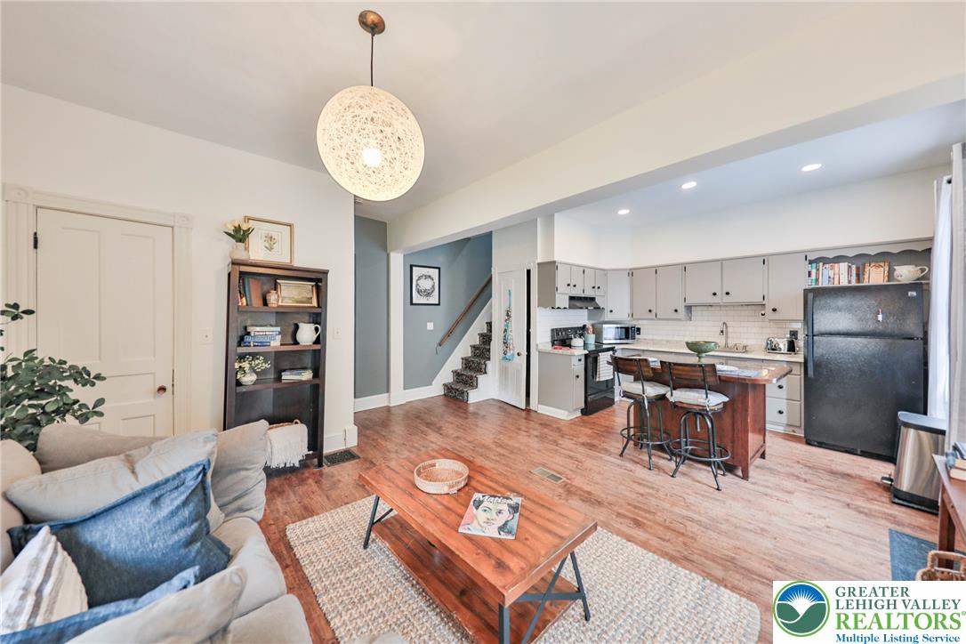 Open-plan living room and kitchen with hardwood floors, a breakfast island, and a staircase.
