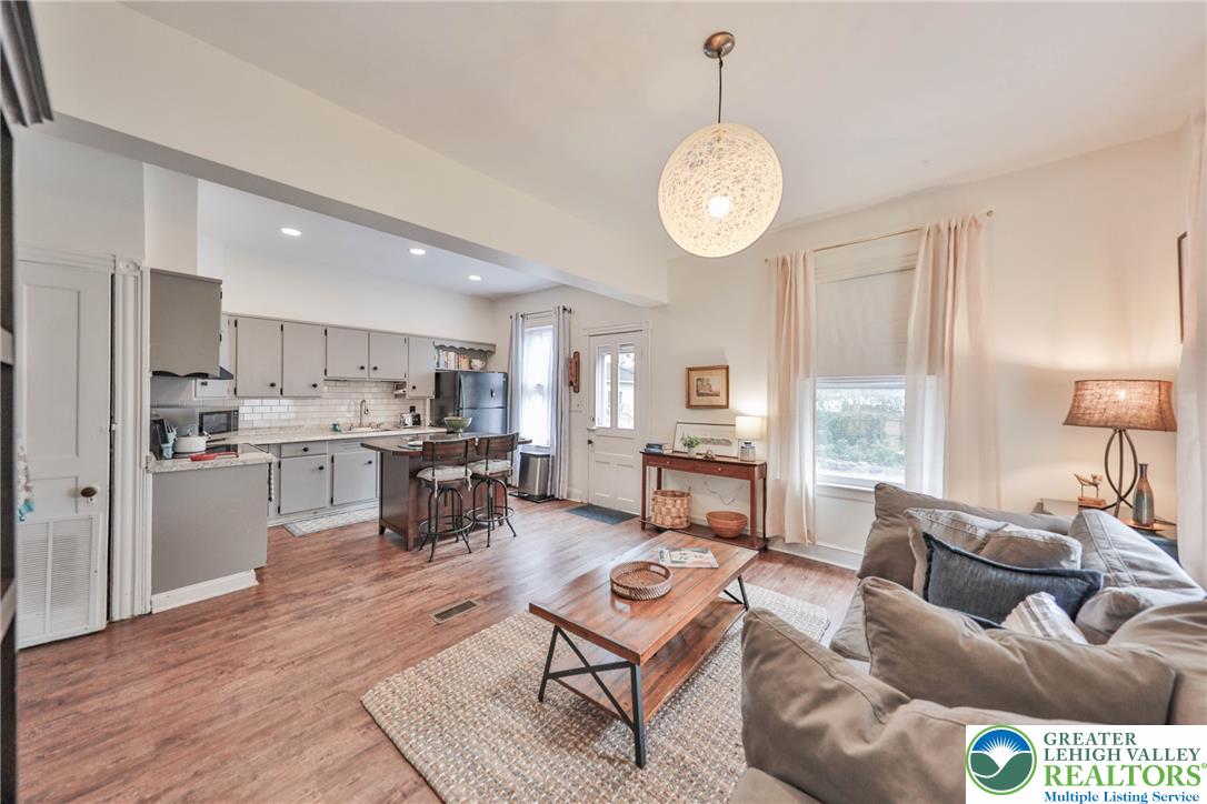 Open kitchen and living room with white cabinetry, island seating, wood floors, and a sofa.