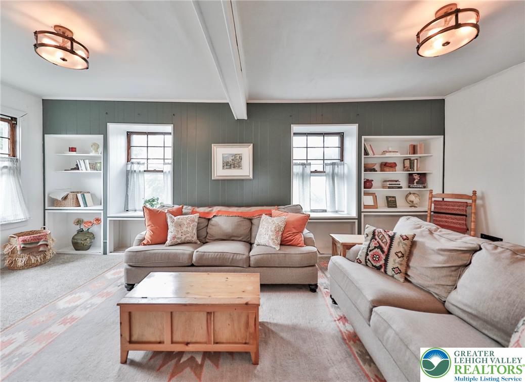 Furnished living room with two sofas, built-in bookshelves, and a muted green paneled accent wall.