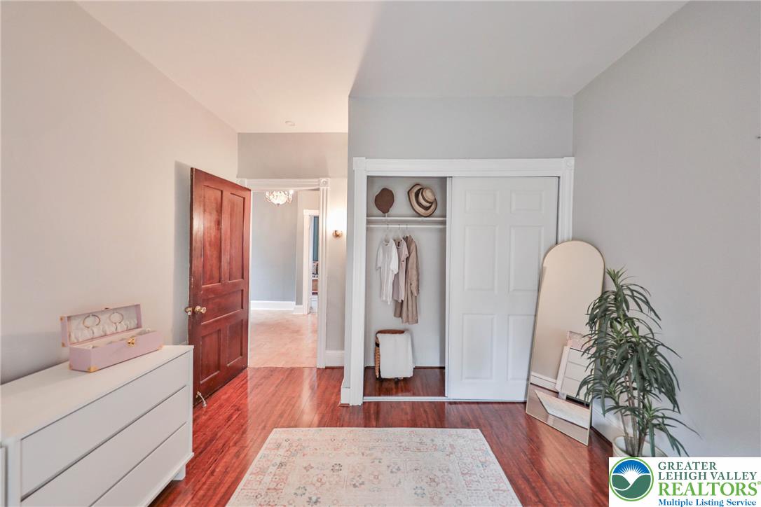 Bedroom with polished hardwood floors, open closet, white dresser, and tall plant.