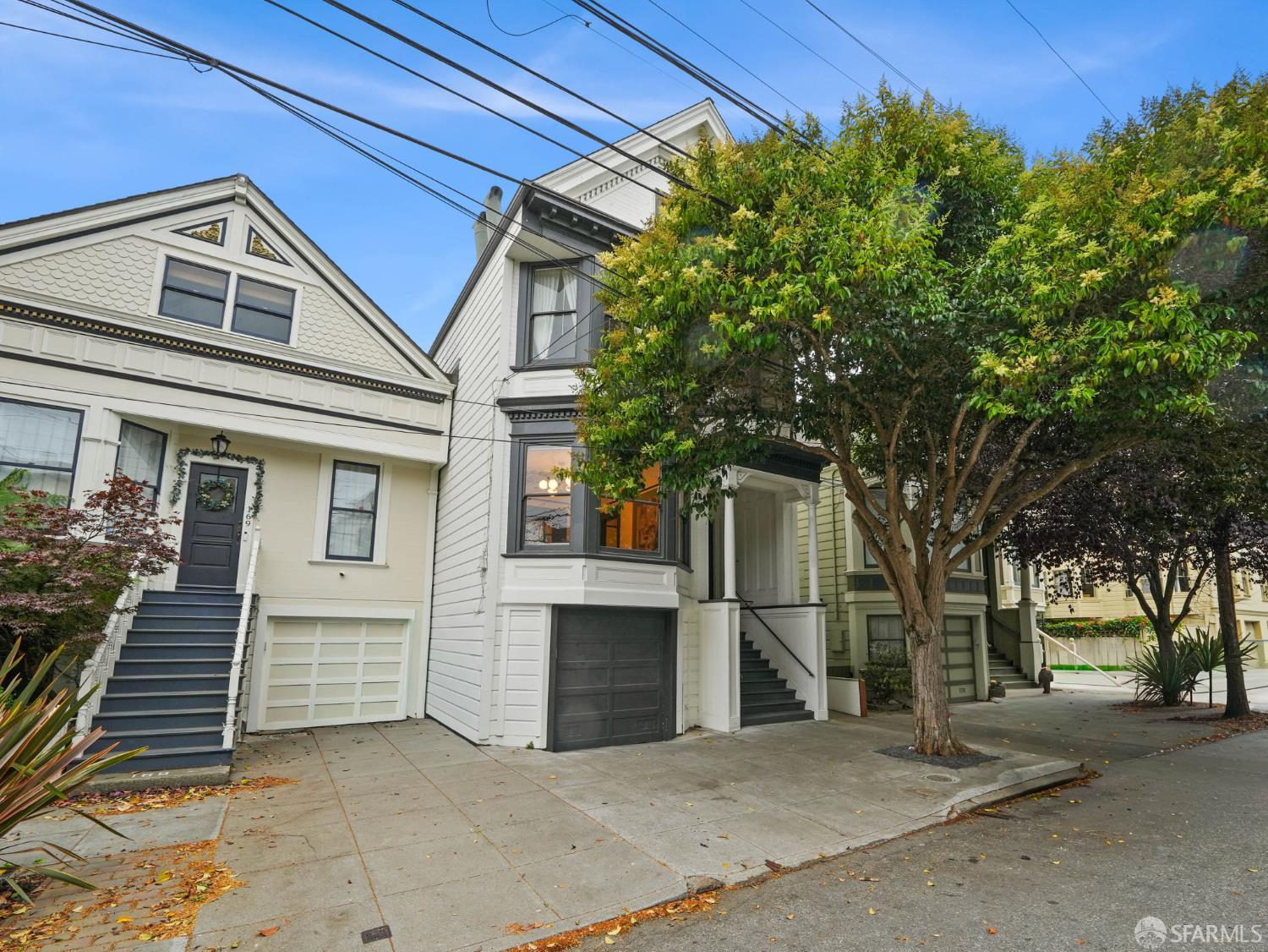 White San Francisco home with a bay window, dark garage door, and leafy tree in front.