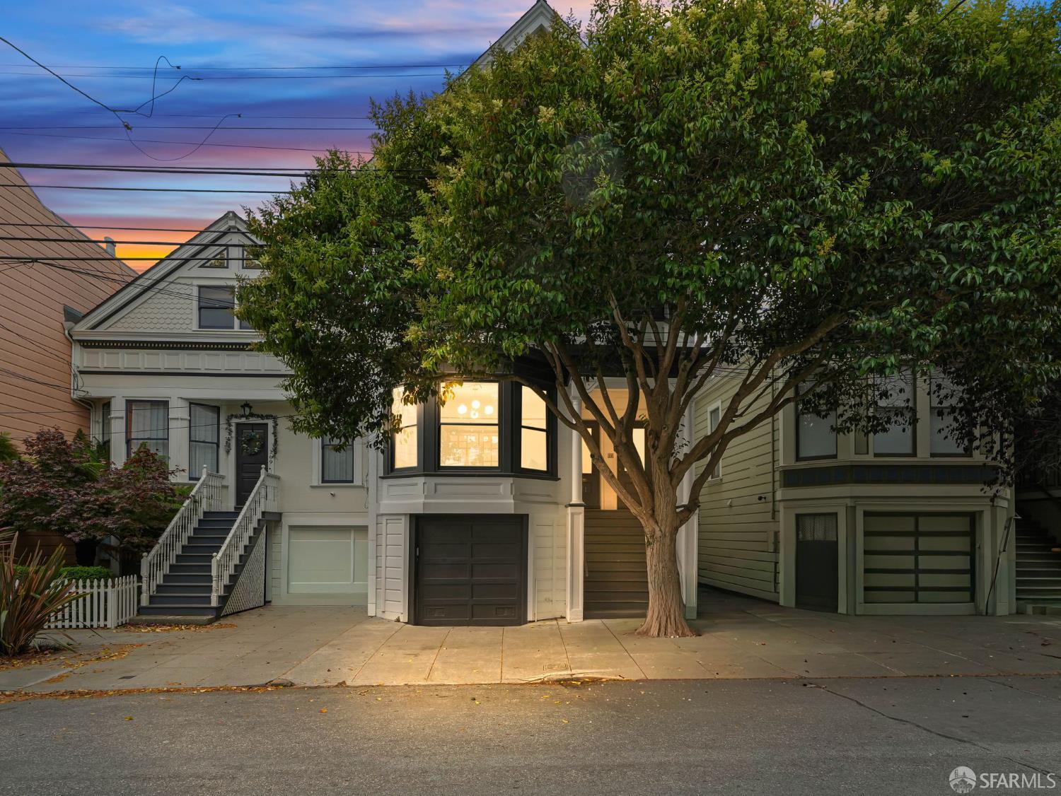 San Francisco home at dusk with illuminated bay windows and a large tree in front.