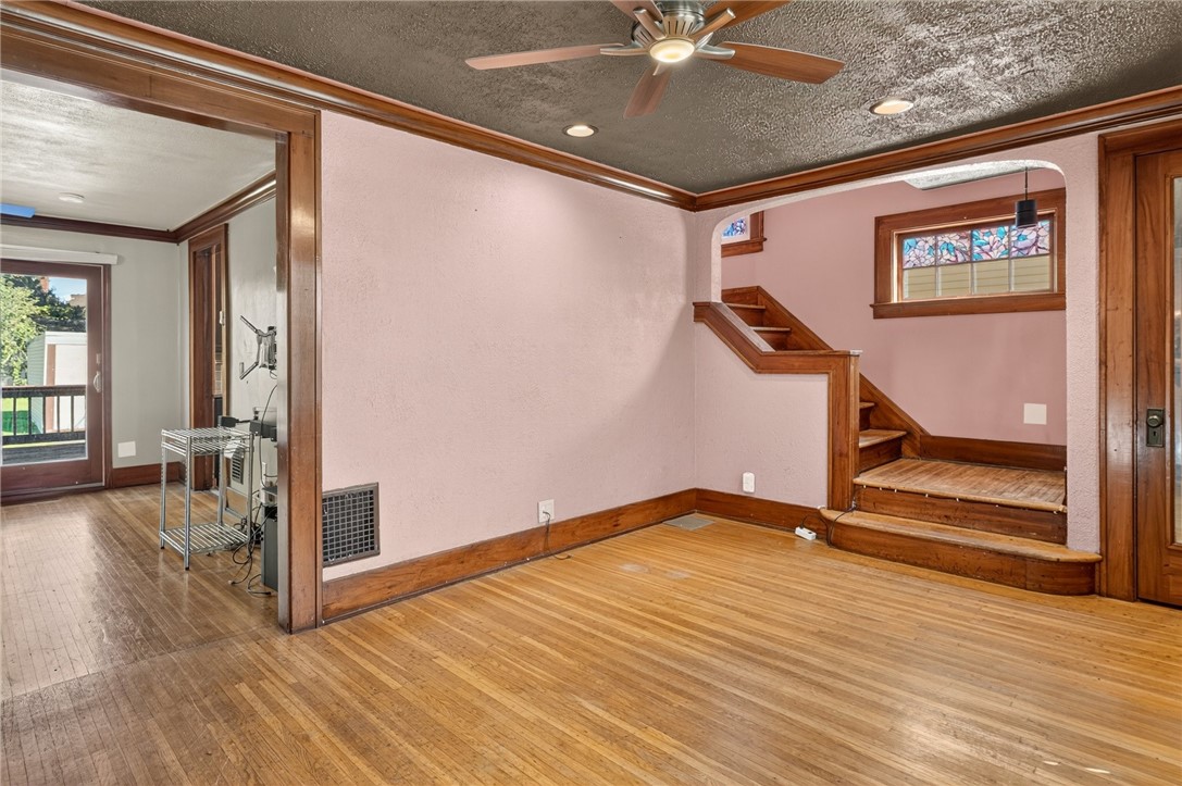 Vacant room with hardwood floors, pink walls, and a raised landing beneath a stained-glass window.
