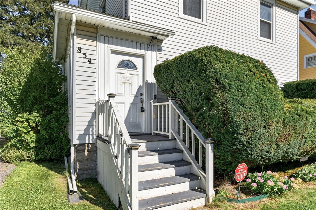House entrance with white-railed stairs, large hedges, and the number 854 beside the door.