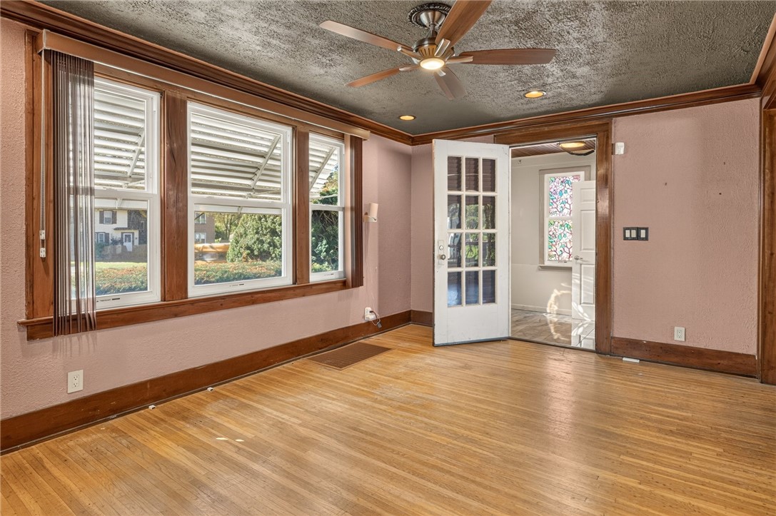 Vacant room with hardwood floors, wide wood-trimmed windows, and a glass-paneled doorway to a stained-glass window.