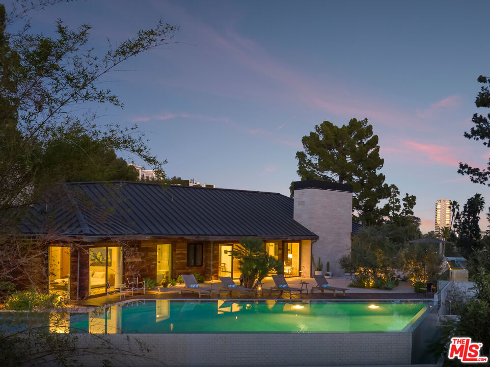Modern home with illuminated windows and a swimming pool at dusk.