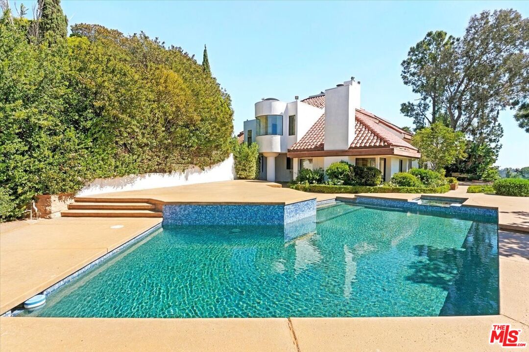 House with a red tile roof and rounded tower behind a large turquoise swimming pool.