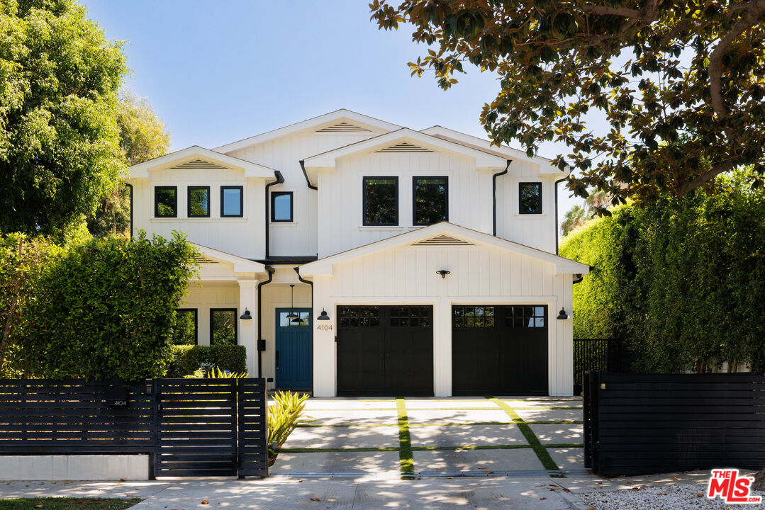 White two-story house with black garage doors, blue front door, and an open black slat fence.