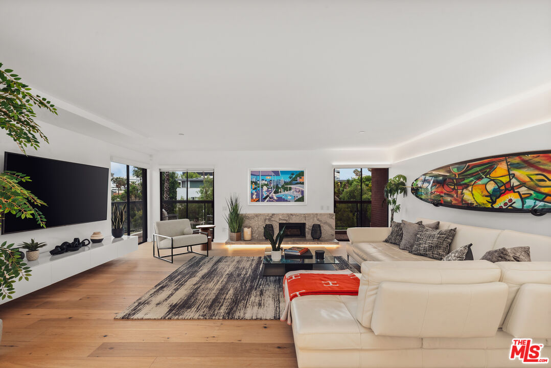 Living room with a white sectional, stone fireplace, and colorful surfboard artwork.