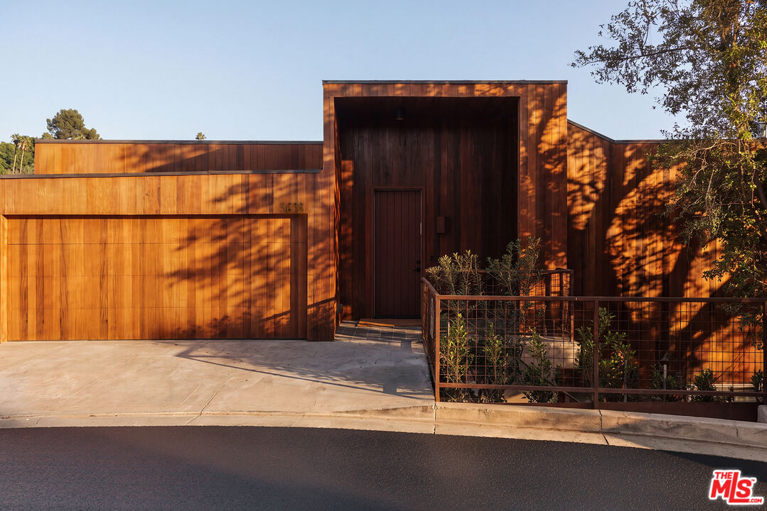 Modern wood-clad home with a recessed entrance, wide garage door, and sunlit facade.