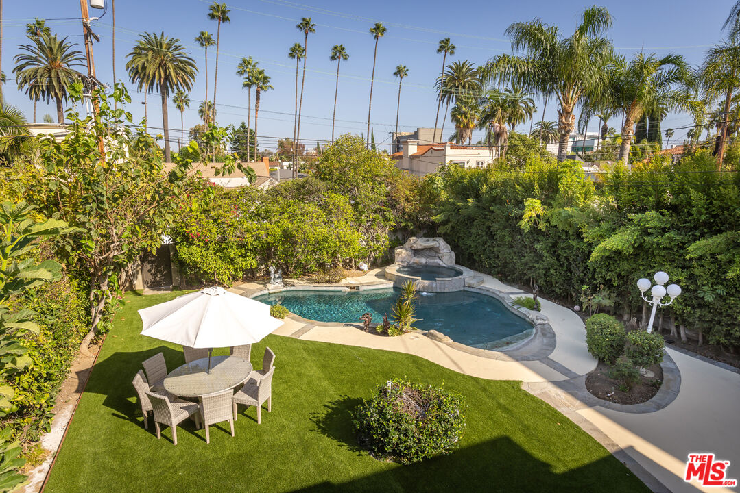 Backyard pool and raised spa beside artificial turf, an umbrella-shaded dining set, and tall palms.