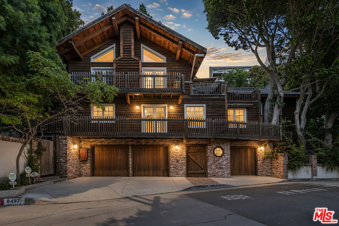 Wood-and-brick home with a steep gable, two balconies, and illuminated windows at dusk.