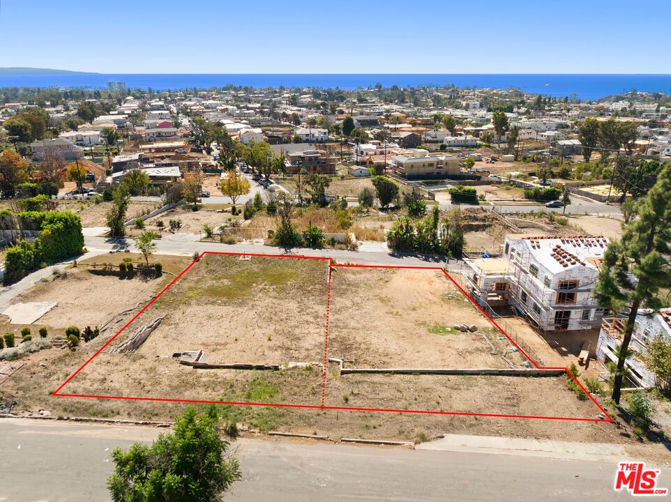 Aerial view of a vacant coastal lot outlined in red, with the ocean beyond.