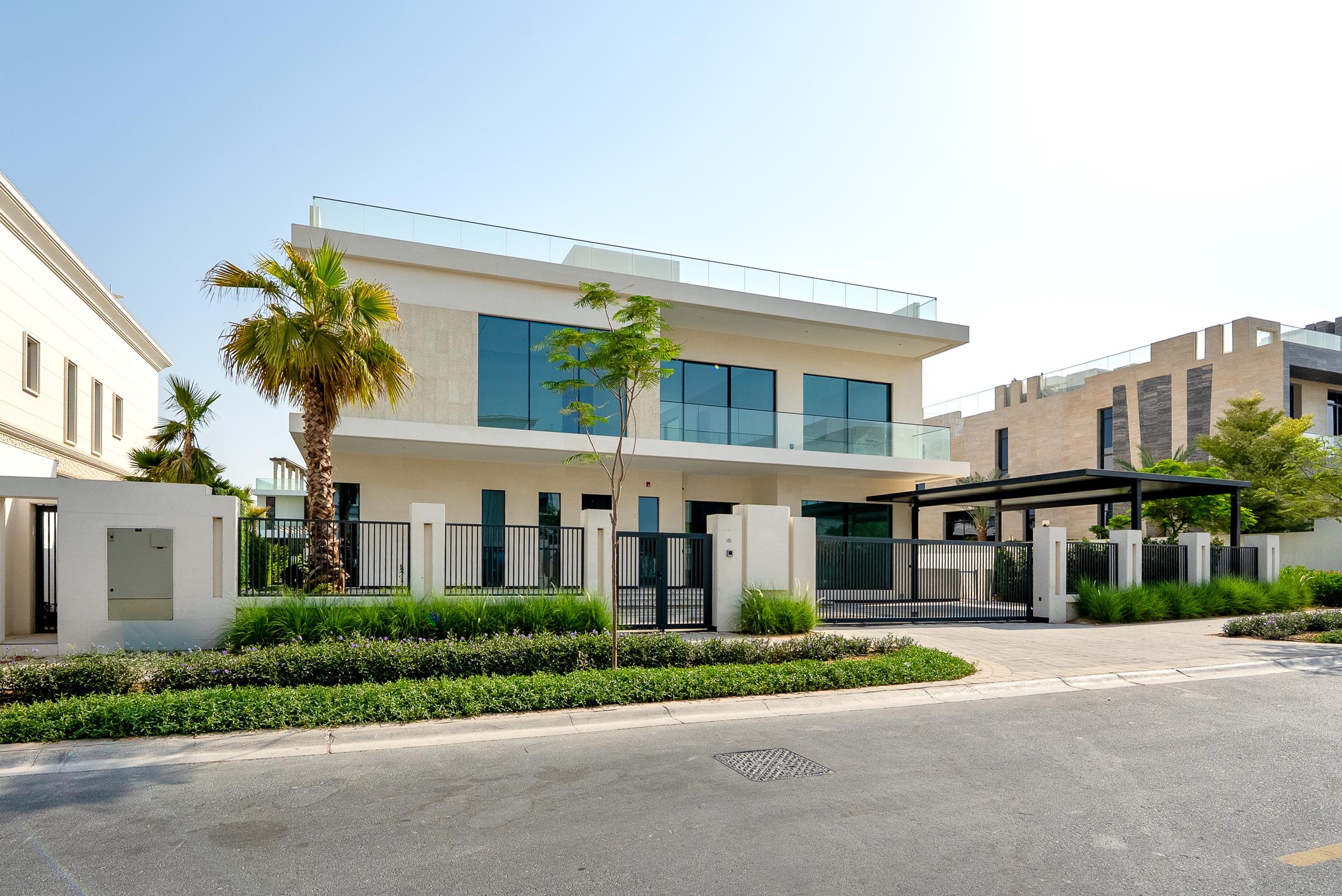 Modern white two-story home with glass balconies, rooftop terrace, gated frontage, and palm landscaping.