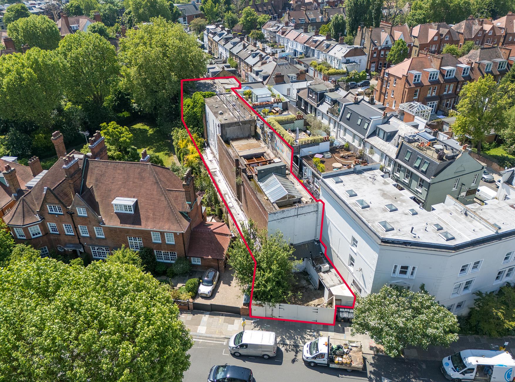 Aerial view of a red-outlined property with rooftop construction among homes and leafy gardens.