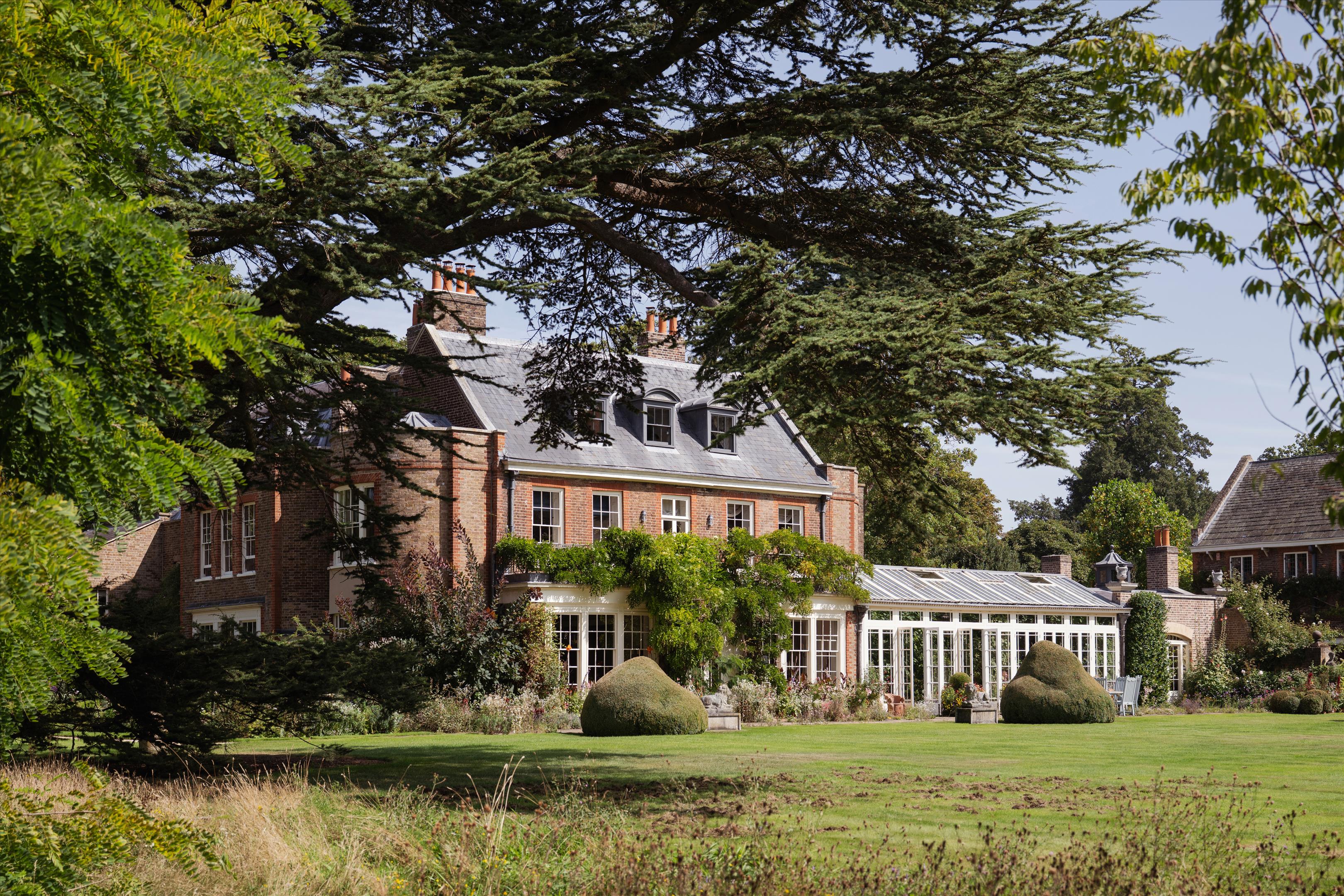 Red-brick residence with slate roof, glass conservatory, and landscaped lawn beneath mature trees.