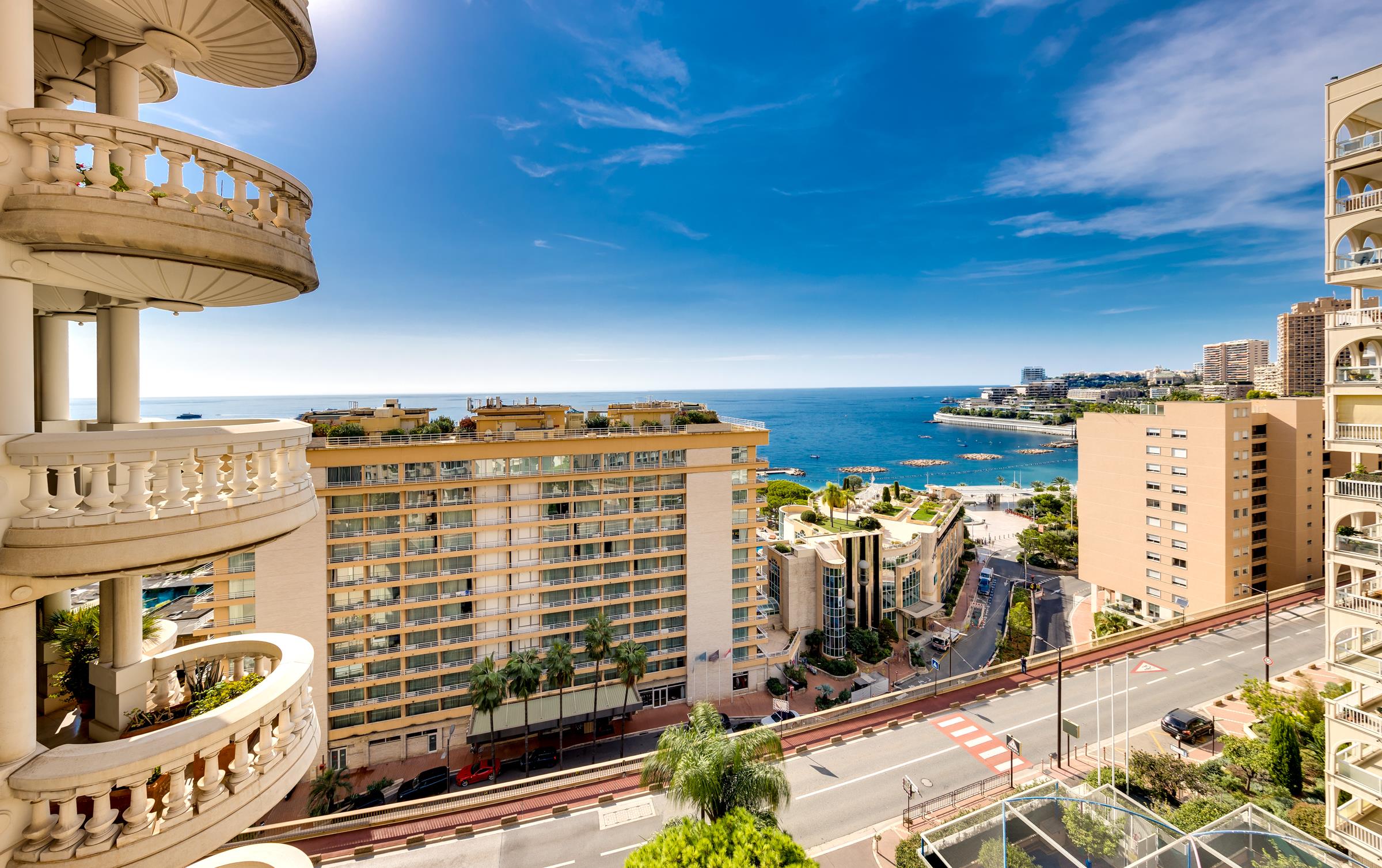 Coastal city view from ornate apartment balconies, overlooking waterfront buildings and the sea.