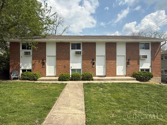 Red-brick residential building with white doors, window air conditioners, and a concrete walkway across the lawn.