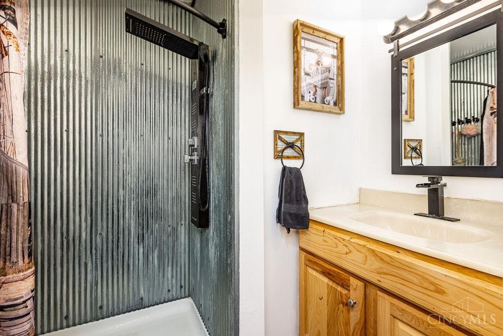 Bathroom with a corrugated metal shower and a wood vanity topped with a cream countertop.