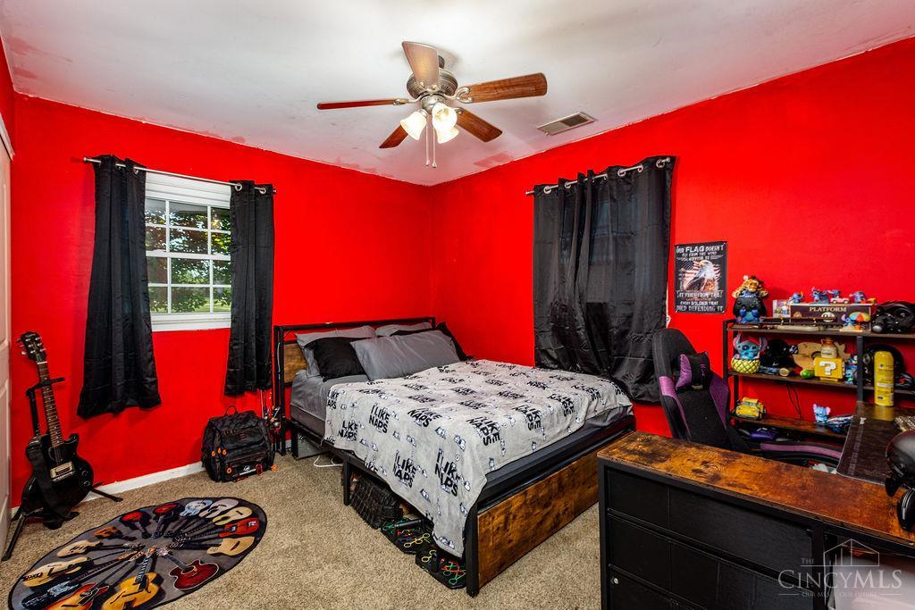 Bedroom with vivid red walls, black curtains, a ceiling fan, and a guitar-themed rug.