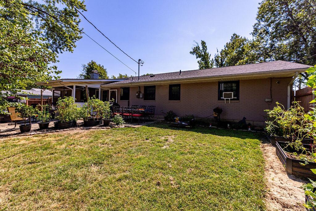 Brick home’s backyard with a covered patio, lawn, and raised garden beds.