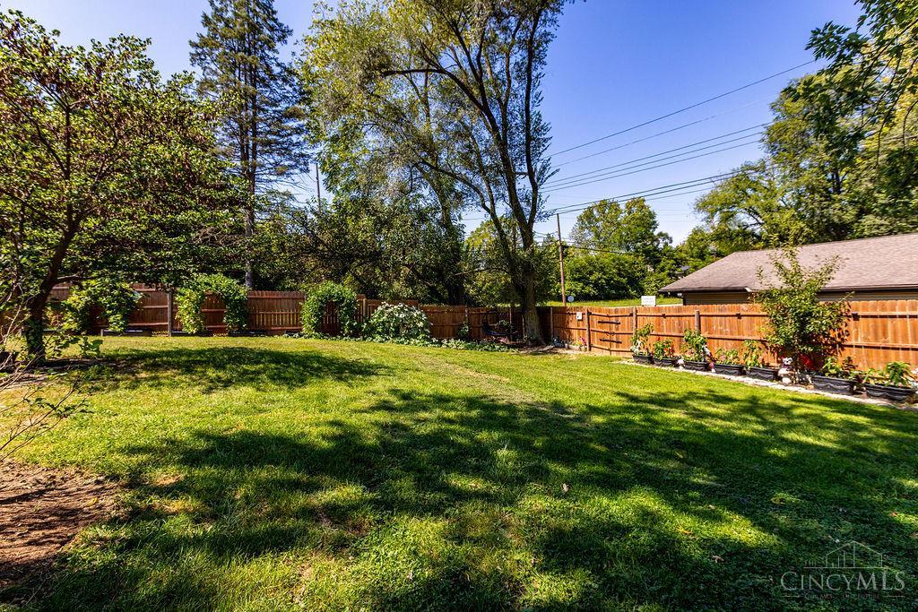 Grassy backyard with mature trees, garden beds, and a wooden privacy fence.