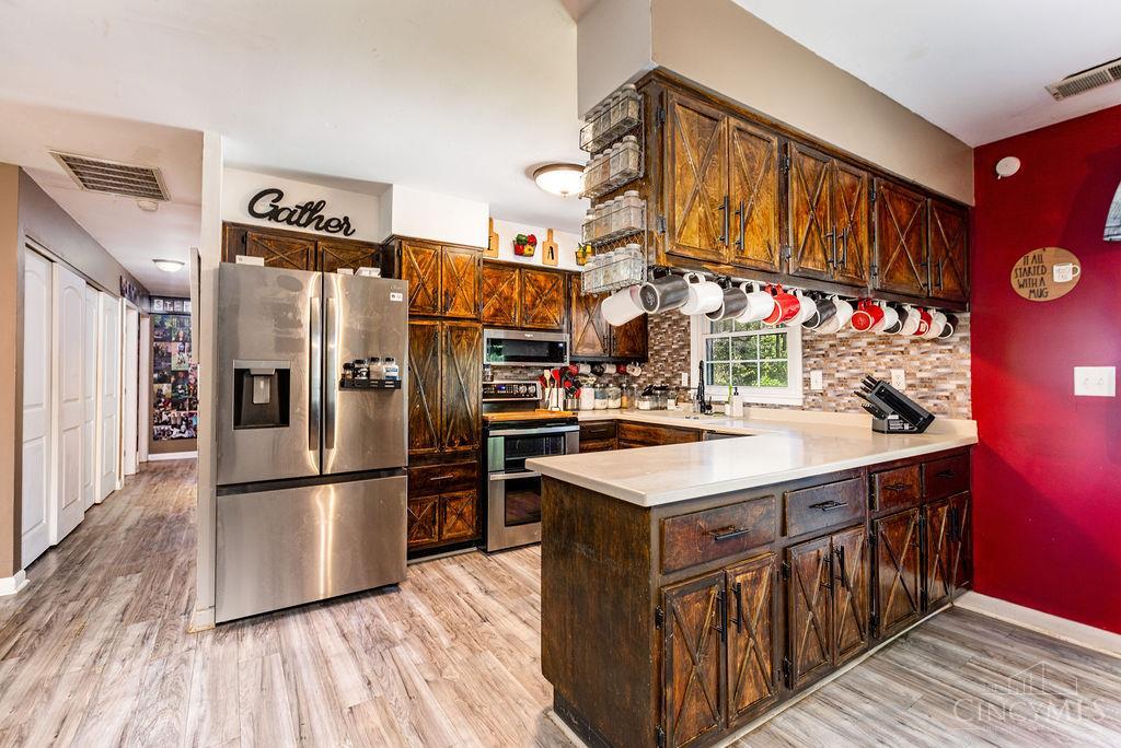 Kitchen with rustic dark wood cabinets, a large island, stainless appliances, and hanging coffee mugs.