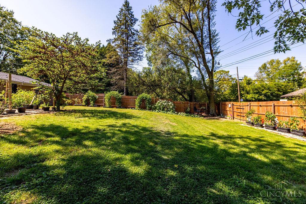 Fenced backyard with a broad lawn, mature shade trees, and garden plants.