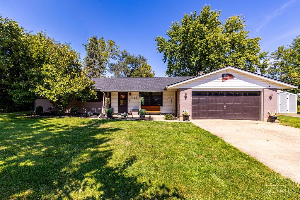 Single-story ranch home with a wide two-car garage, shaded lawn, and mature trees.