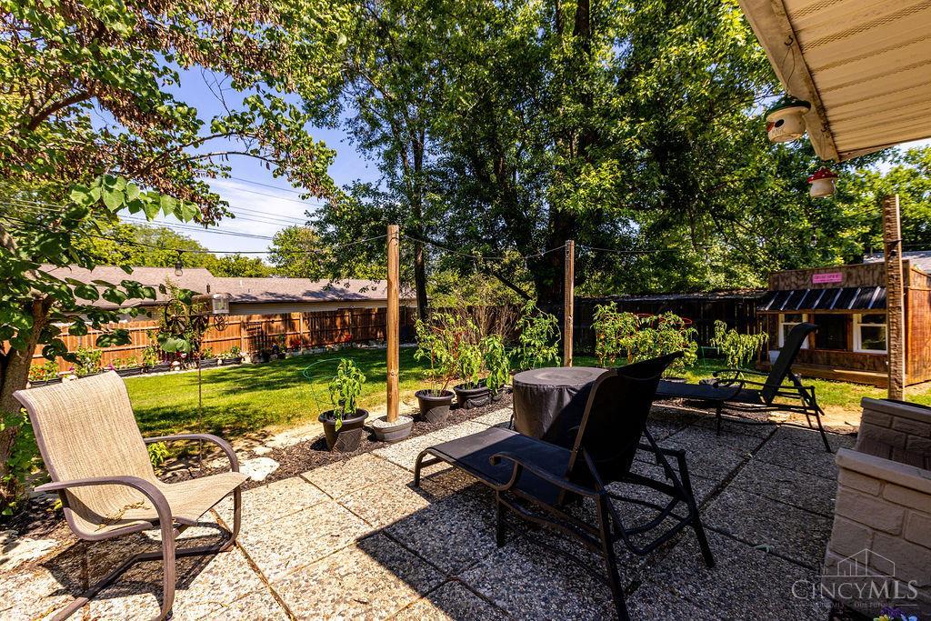 Backyard patio with outdoor seating, potted plants, and a lawn shaded by mature trees.