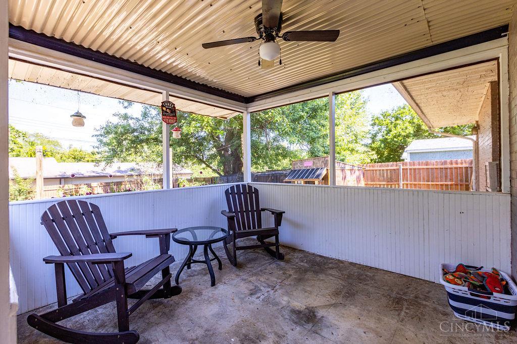 Screened-in porch with two Adirondack chairs, a round table, and a ceiling fan.