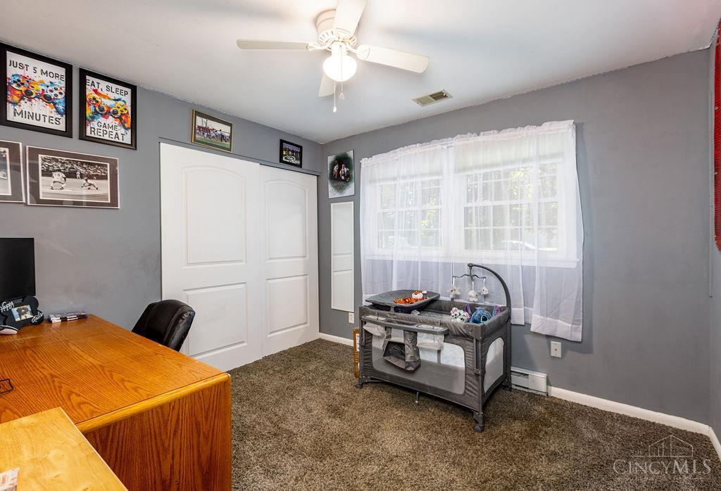 Bedroom with gray walls, white closet doors, a wooden desk, and a baby play yard by the window.