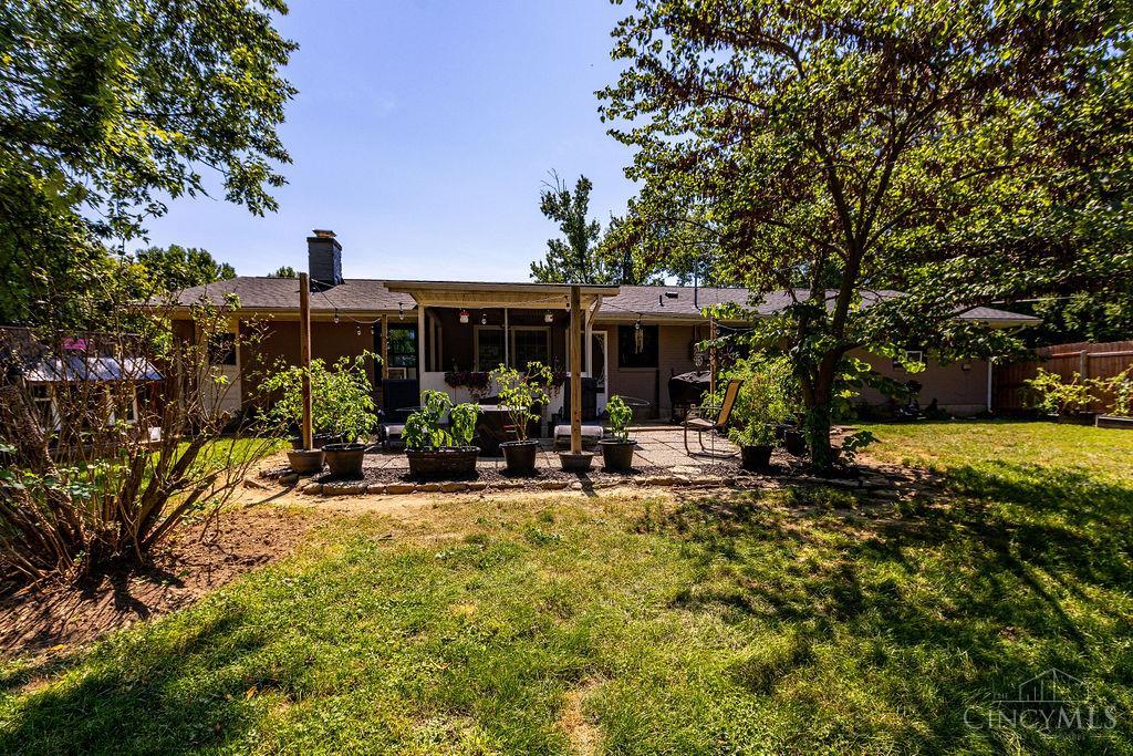 Single-story home with a covered patio, potted plants, mature trees, and a sunny backyard lawn.