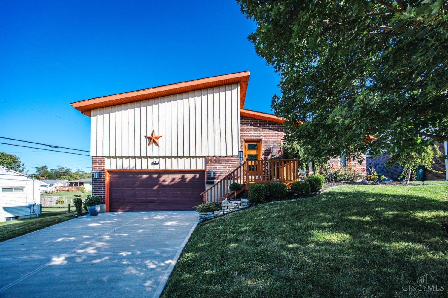 Split-level brick and white-sided home with a two-car garage, wooden entry deck, and sloping lawn.