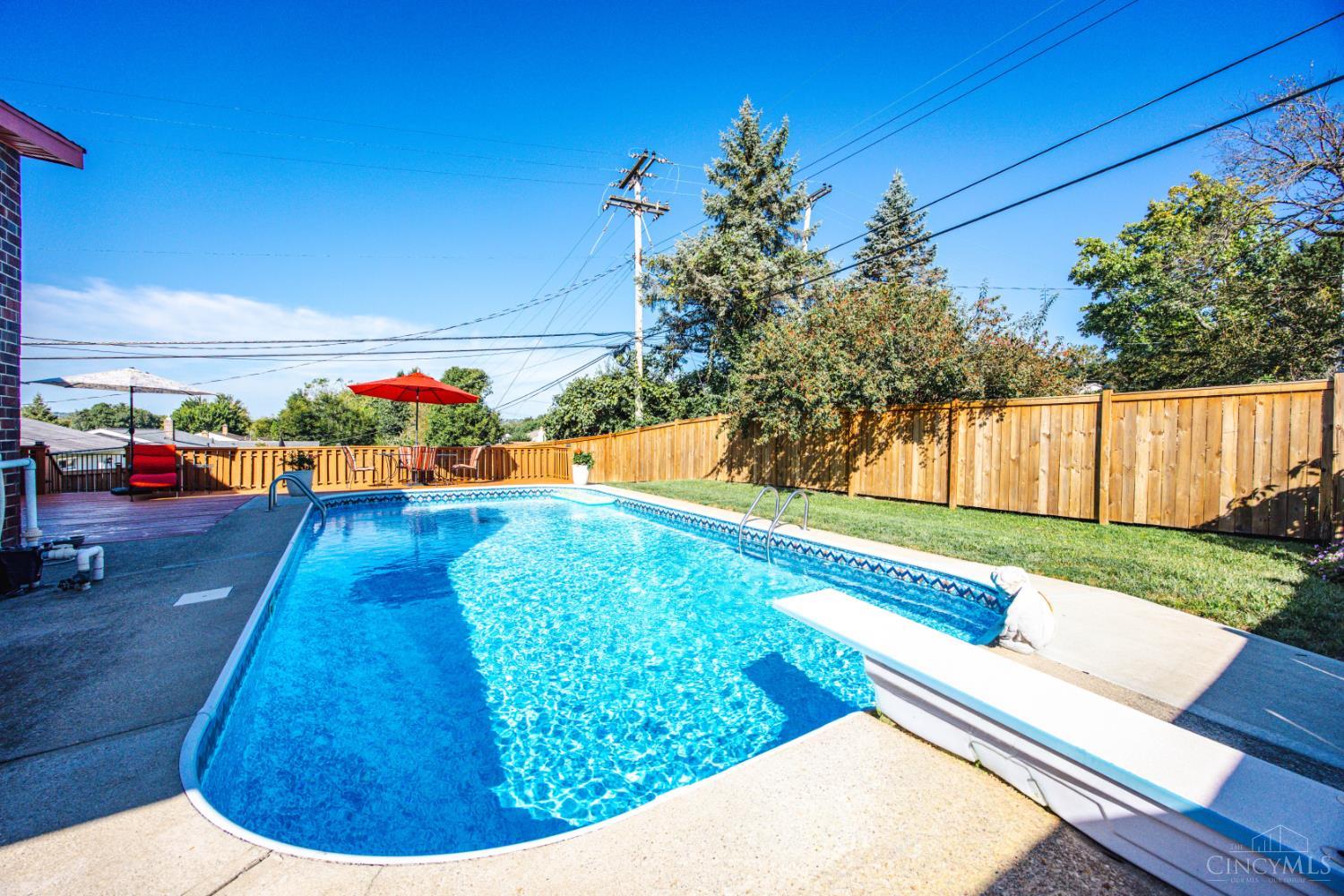 Backyard swimming pool beside a fenced patio and deck with red umbrellas.