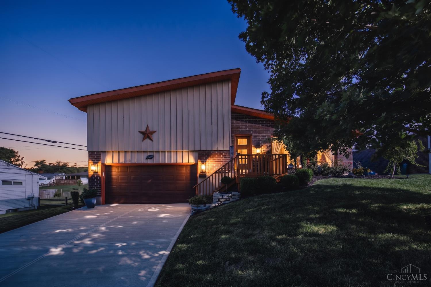 Modern home at dusk with a brick facade, star decoration, and broad concrete driveway.