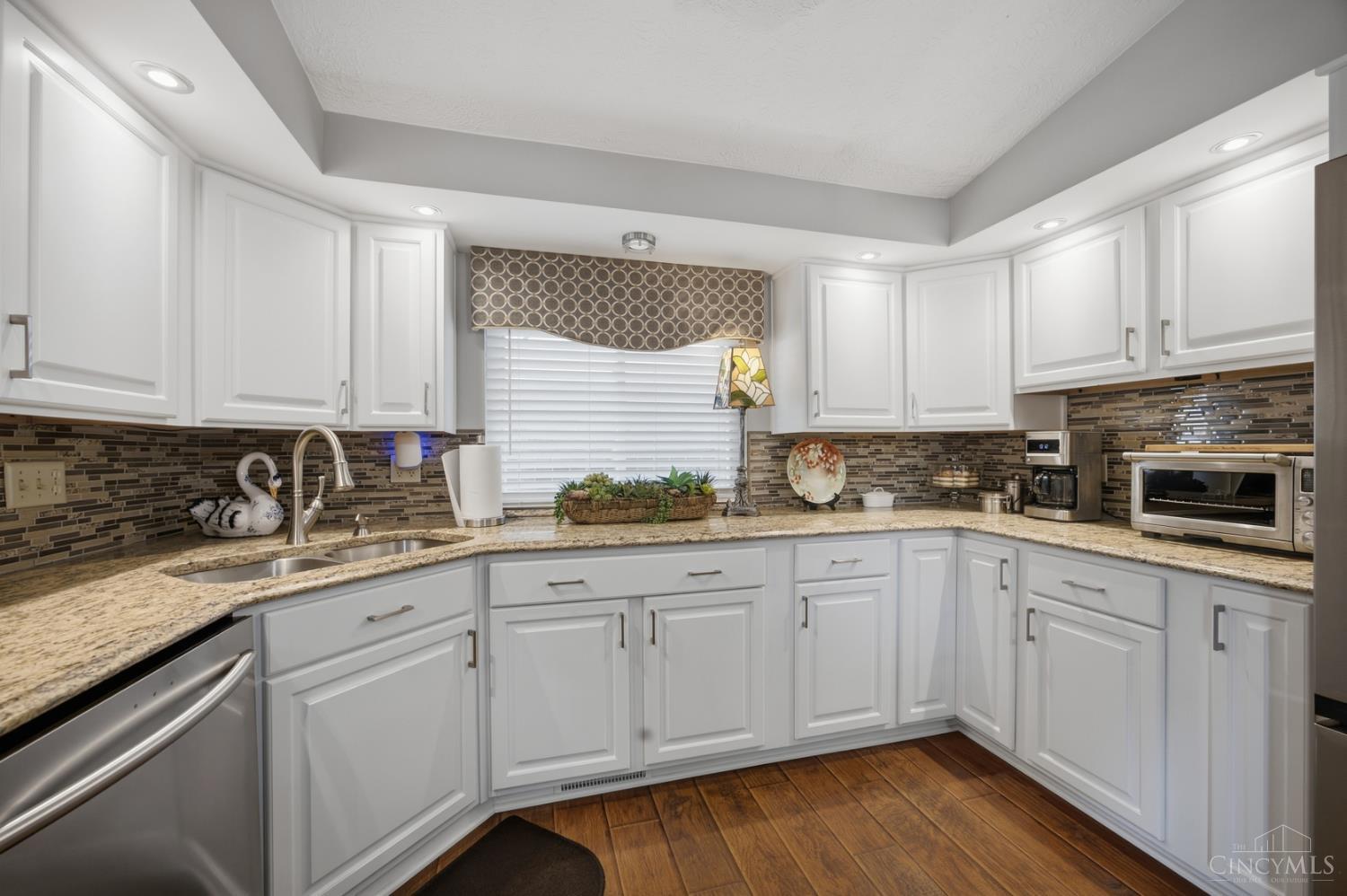 Kitchen with white cabinets, granite counters, mosaic backsplash, and stainless-steel appliances.