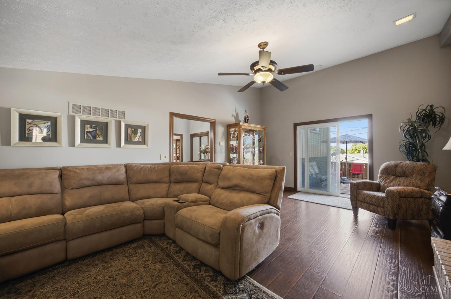 Living room with a tan sectional, matching recliner, ceiling fan, and sliding doors to a deck.