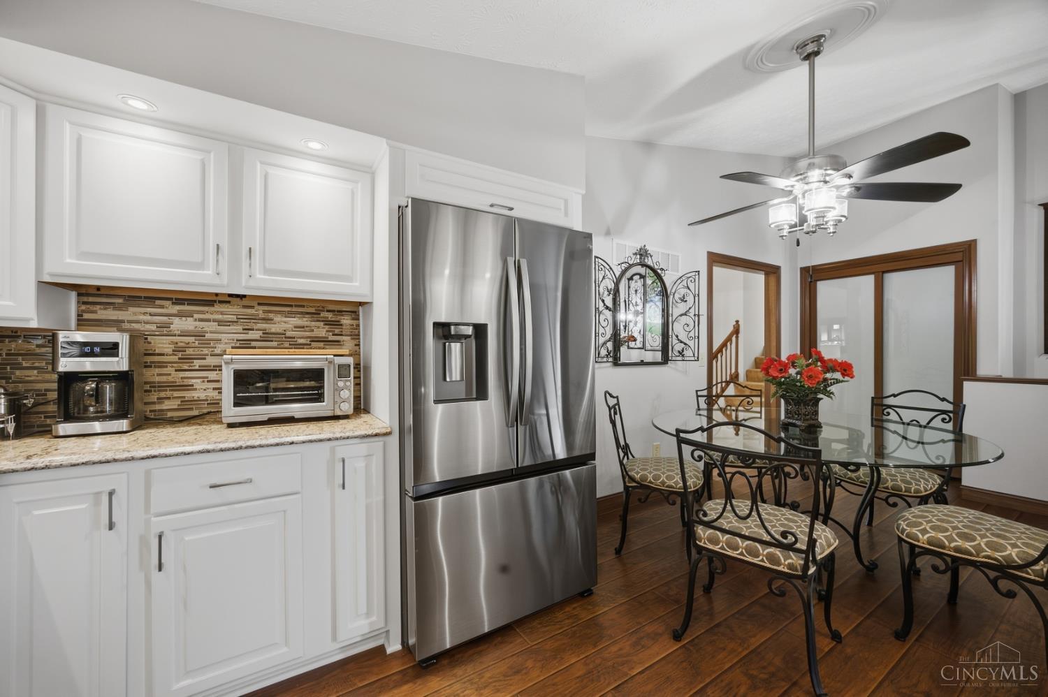 Kitchen with white cabinets, stainless appliances, mosaic backsplash, and an adjoining glass dining table.