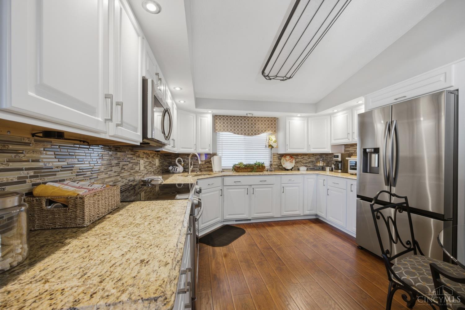 Kitchen with white cabinetry, granite counters, mosaic backsplash, stainless steel appliances, and wood-look flooring.