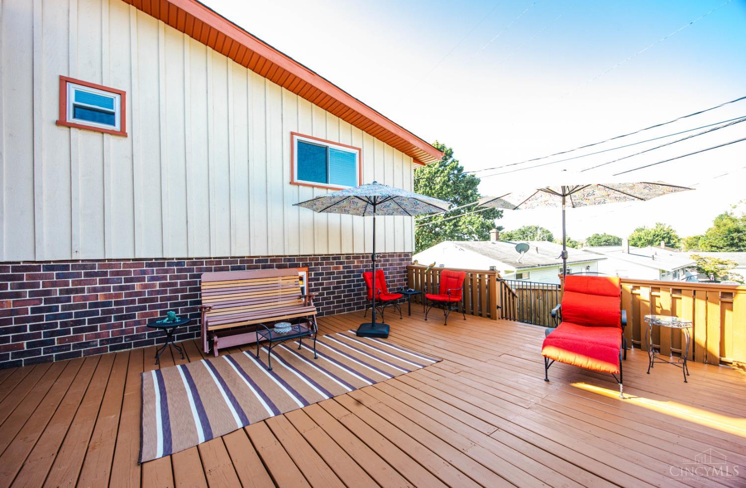 Furnished wooden deck with red-cushioned chairs, a bench, striped rug, and patio umbrellas.