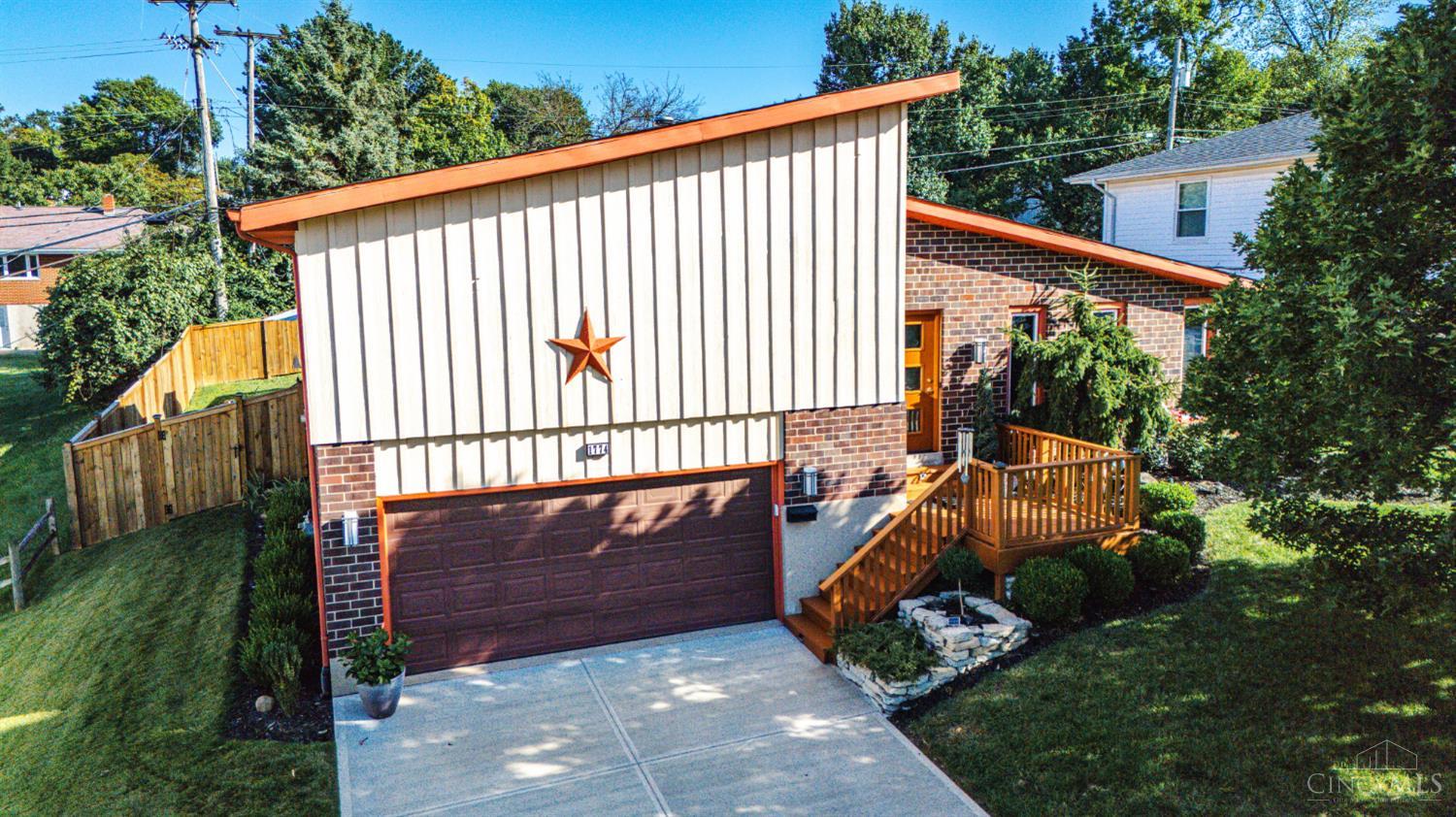 Split-level home with cream siding, brick accents, orange trim, and a raised wooden porch.