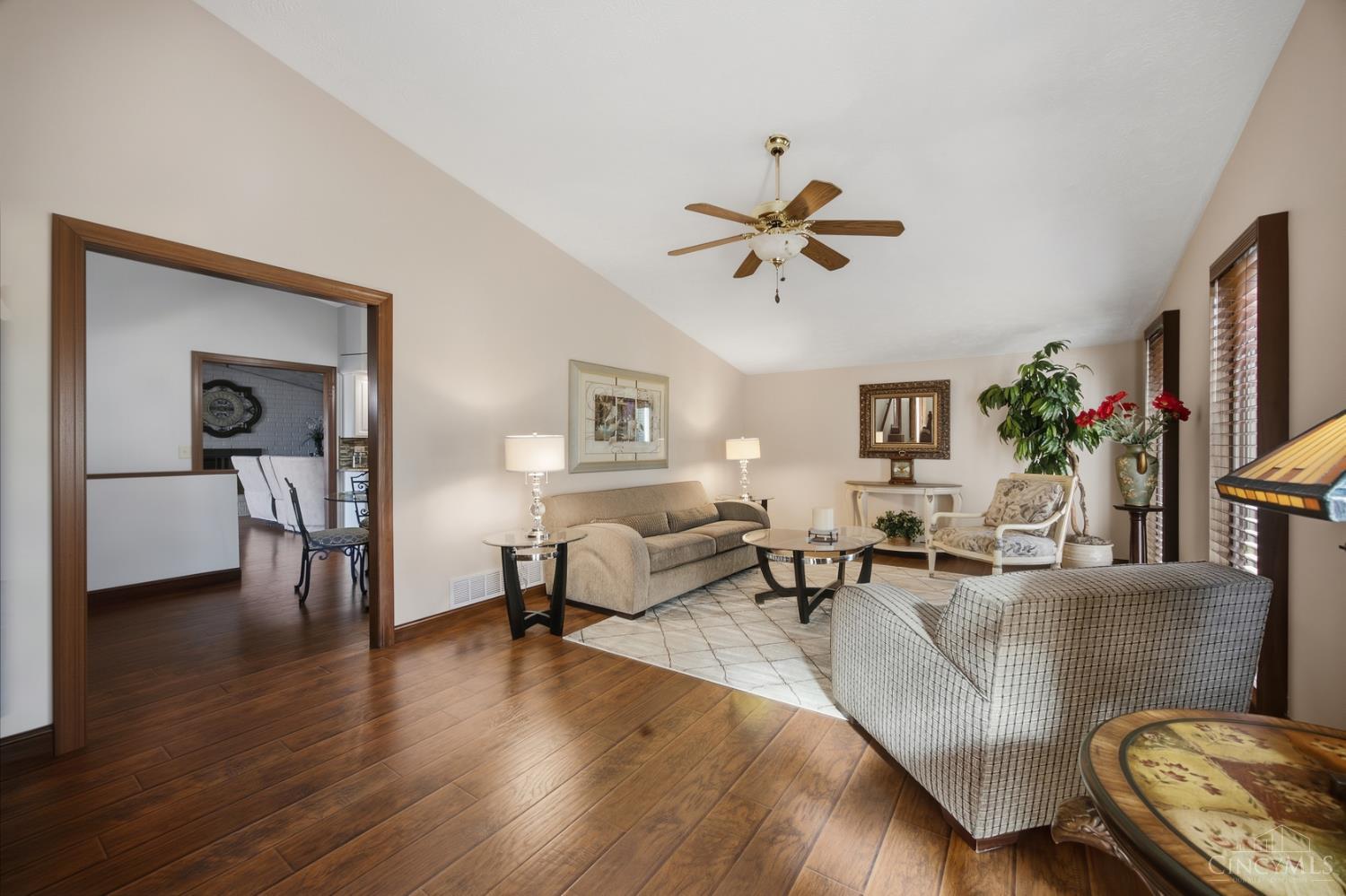 Living room with a beige sofa, patterned armchair, hardwood floors, and a ceiling fan.
