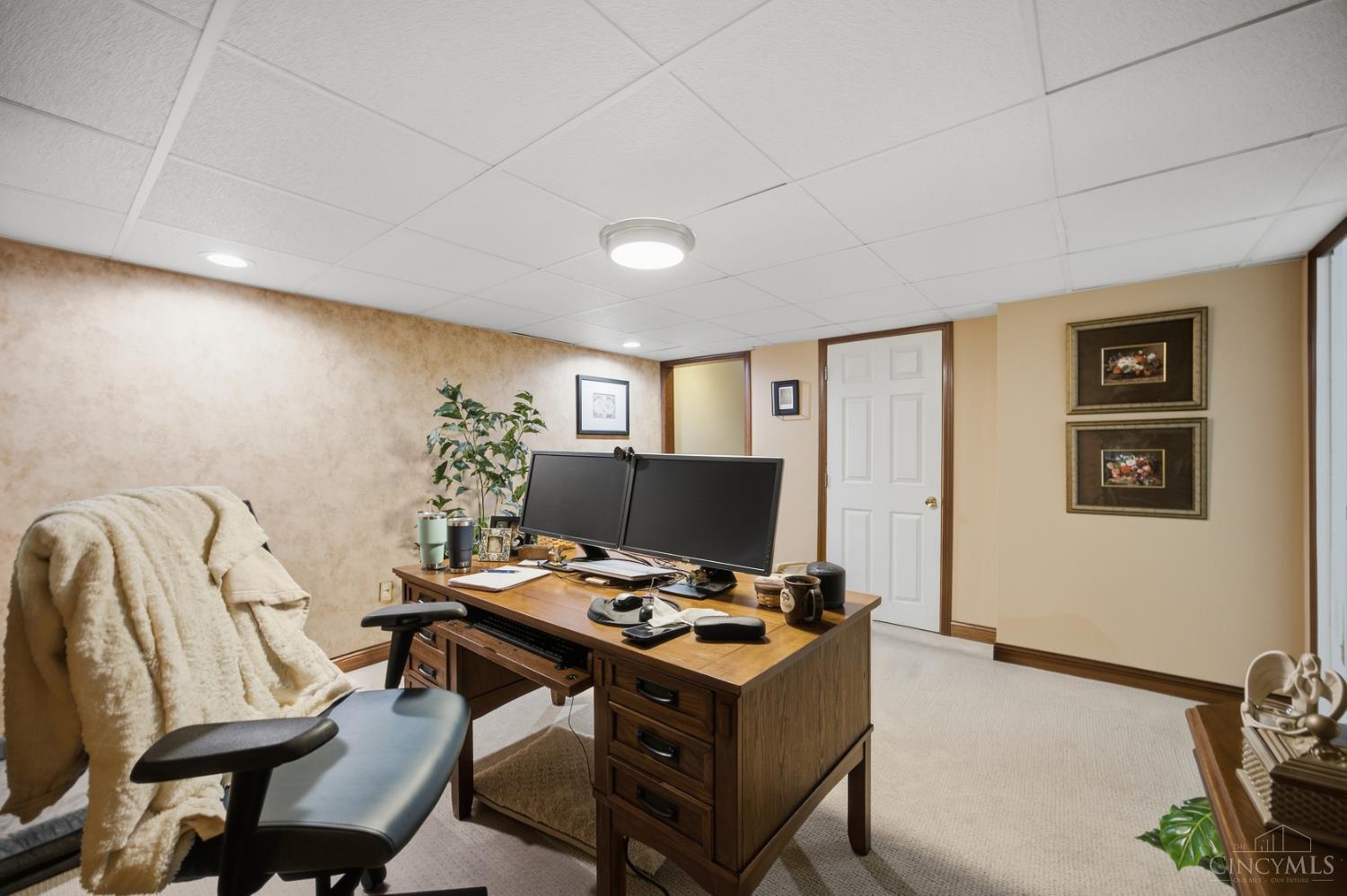 Furnished home office with a wooden desk, dual monitors, and a blanket-draped chair.