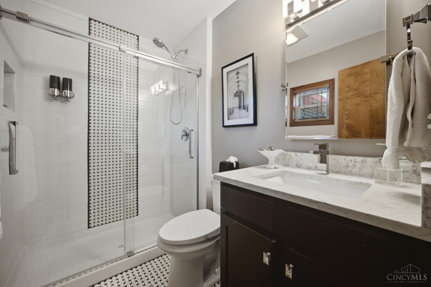 Bathroom with glass shower, mosaic tile accent, toilet, and dark vanity with marble countertop.