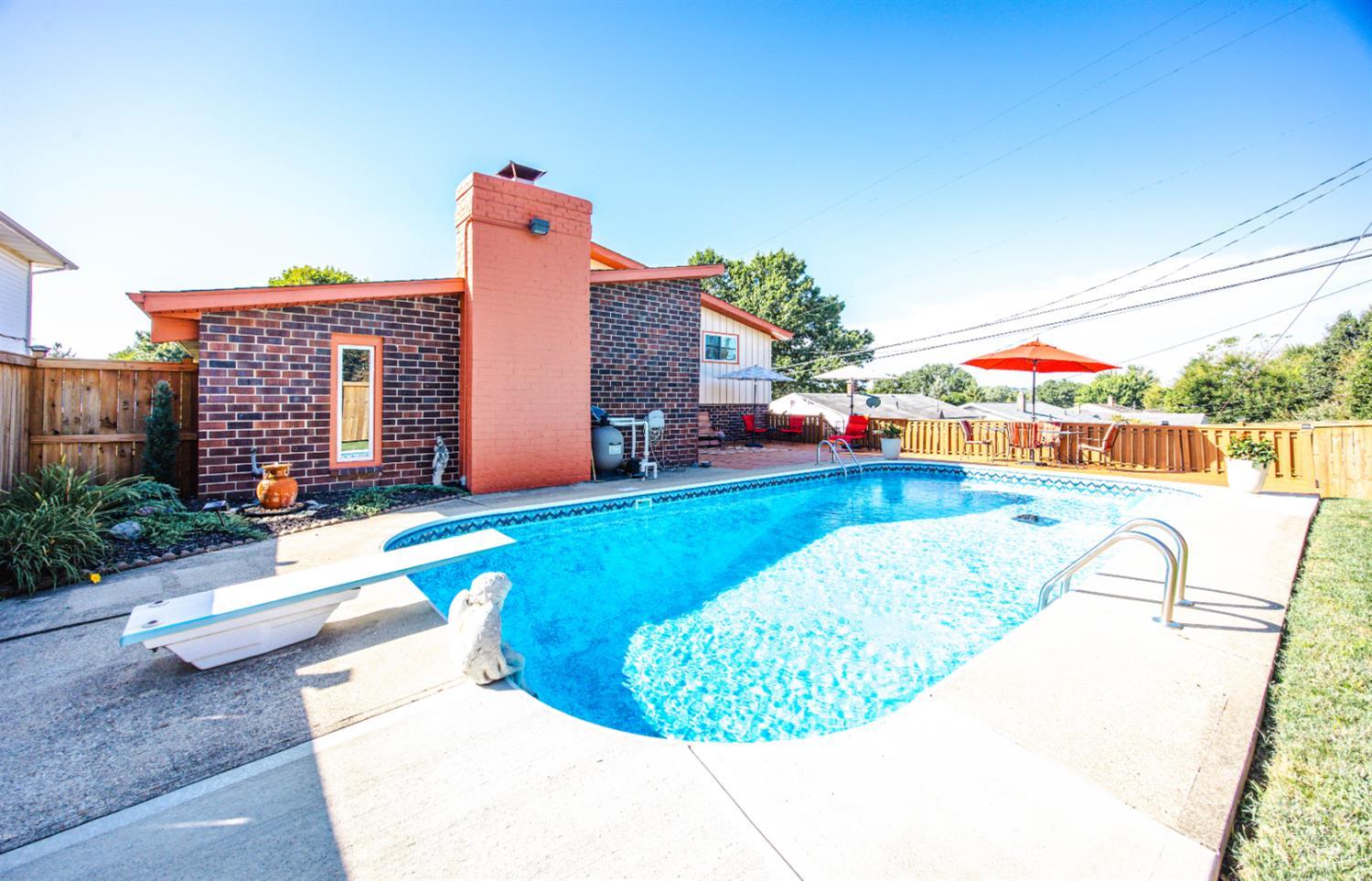 Backyard swimming pool with a diving board beside a dark brick home and fenced patio.
